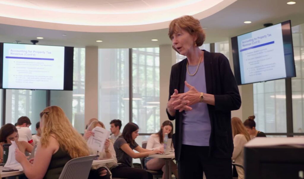 A professor engages with students in a brightly lit modern classroom